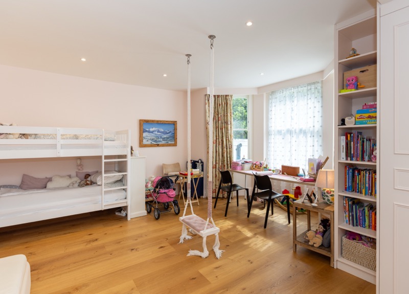 Children's bedroom with white bunk bed, rope swings, study desks and built-in bookshelves beneath a bay window