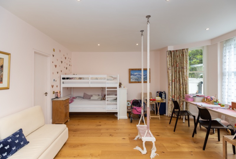 Children's bedroom with white bunks, heart-print feature wall and craft desks beside a bay sash window