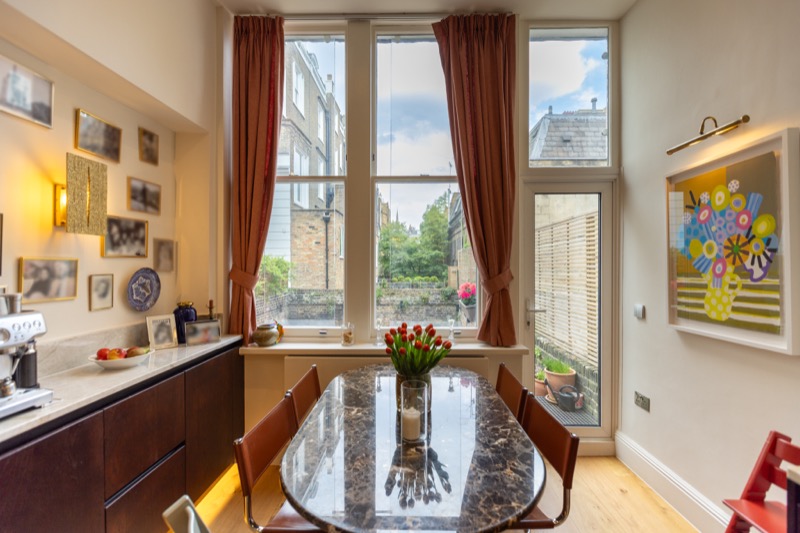 Compact dining nook with oval marble table, gallery wall of family photographs and tall garden-facing window