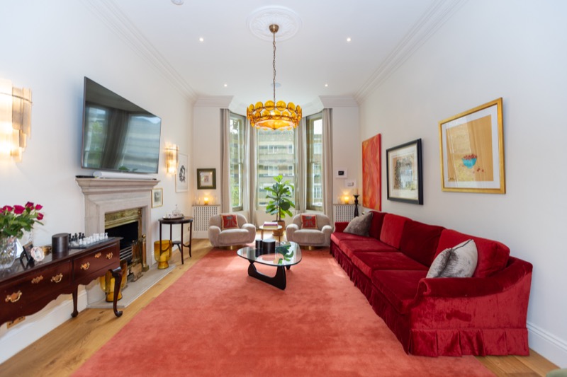 Period reception room with red velvet sofa, marble fireplace and bay sash windows framing curated artwork