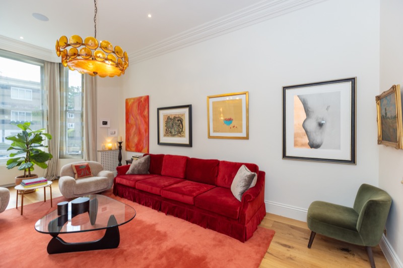 Long red velvet sofa beneath a gallery of contemporary art with chartreuse Murano-glass pendant chandelier