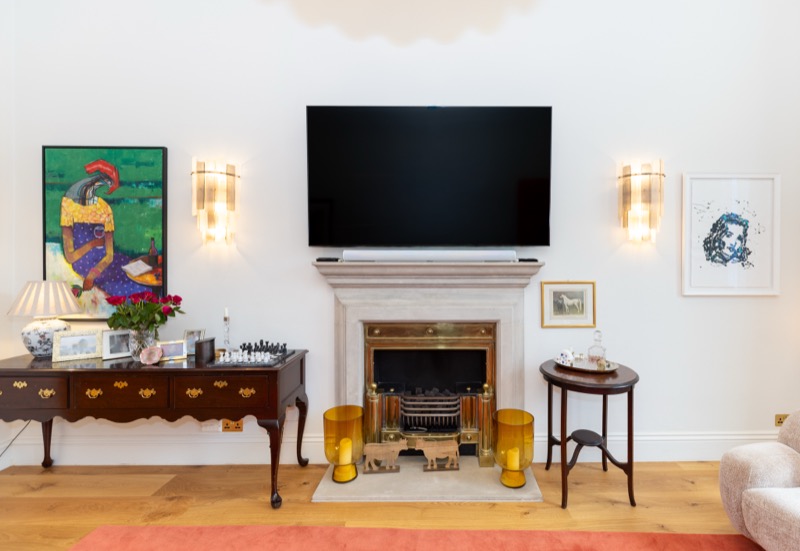 Mounted television above a carved stone fireplace flanked by crystal wall sconces and an antique console