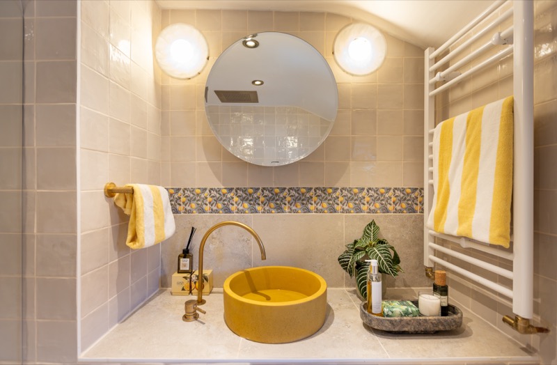 Bathroom with yellow concrete basin, brass tap, Mediterranean lemon-tile border and heated towel rail