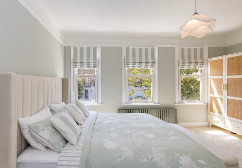 Principal bedroom with three sash windows, striped Roman blinds, upholstered headboard and sage walls