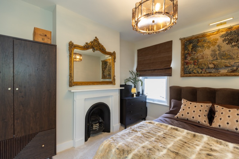 Bedroom with dark timber wardrobe, gilt mirror over a fireplace and antique woven tapestry above the bed