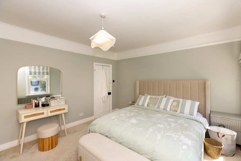 Bedroom with cane dressing table, arched brass mirror and upholstered bed against soft sage walls
