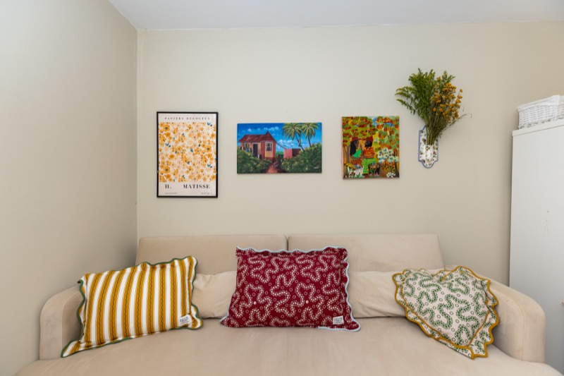Children's bedroom with framed Matisse and folk-art prints above embroidered cushions on a neutral bed