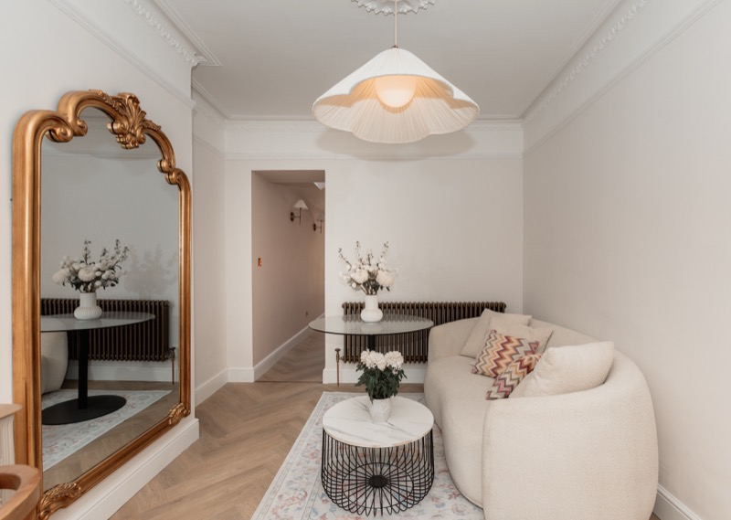 Hallway nook with gold rococo mirror, dark console, white boucle sofa and ruched pendant lampshade