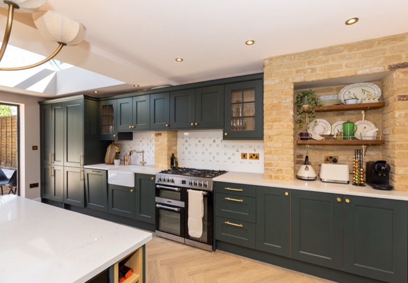 Range cooker beneath an exposed brick chimney breast with brass-handled Shaker cabinetry