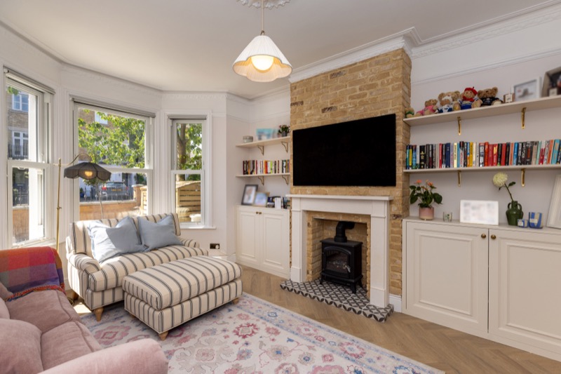 Living room with built-in alcove joinery, exposed brick chimney, cast-iron woodburner and sash bay window