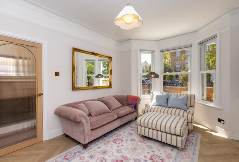 Front sitting room with pink velvet sofa, striped armchair, bay sash window and ornate gilt mirror
