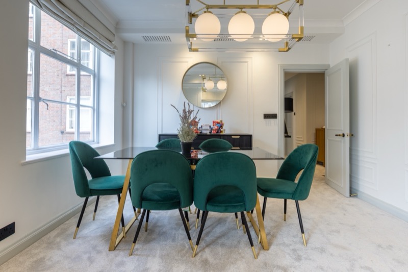 Elegant dining room with emerald chairs and round mirror